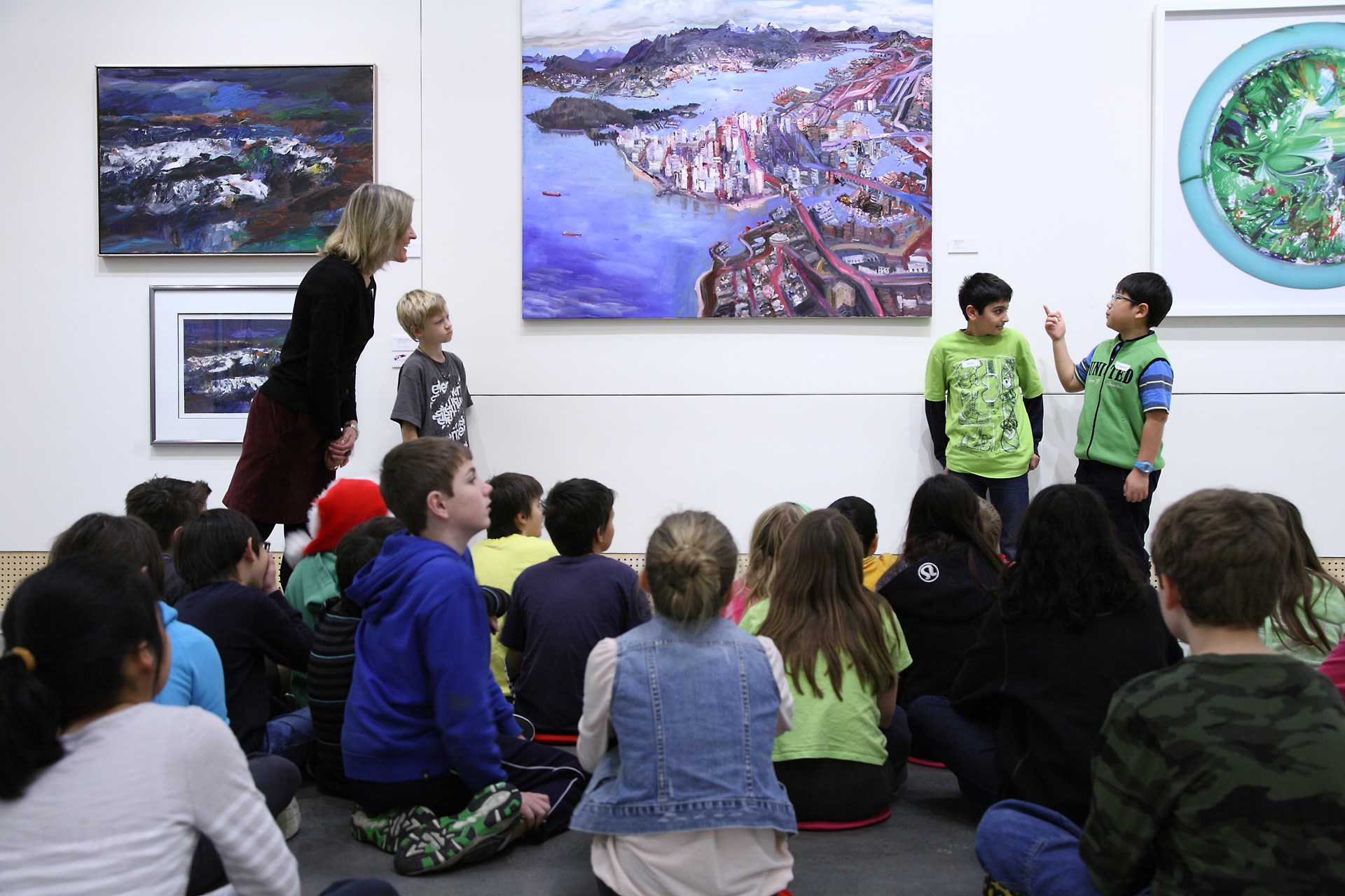 In the GS Gallery, two students talk about a painting while a class of students and a teacher look on