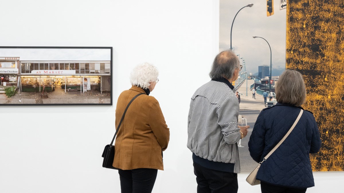 Three older adults looking closely at a exhibition piece in the Gordon Smith Gallery